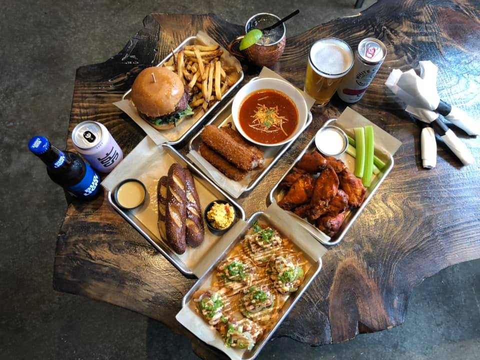 A table spread of Nona Social burgers, jumbo wings, mozz sticks, tostones and draft beer